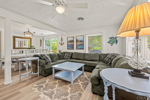 living room featuring visible vents, ornamental molding, wood finished floors, a textured ceiling, and ceiling fan with notable chandelier