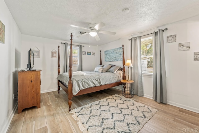 bedroom with baseboards, multiple windows, a textured ceiling, and light wood finished floors