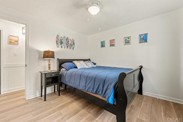 bedroom featuring light wood-style floors, a wainscoted wall, and ceiling fan