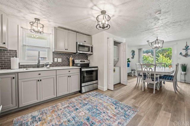 kitchen featuring a chandelier, stacked washer and dryer, a sink, light countertops, and appliances with stainless steel finishes