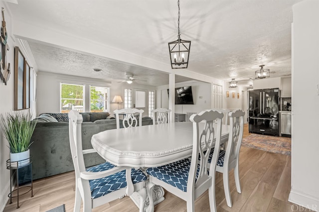 dining room featuring light wood finished floors, a textured ceiling, and ceiling fan with notable chandelier