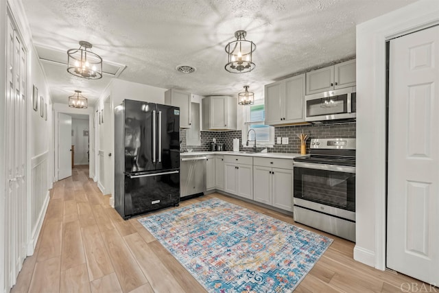 kitchen with an inviting chandelier, stainless steel appliances, light countertops, pendant lighting, and a sink