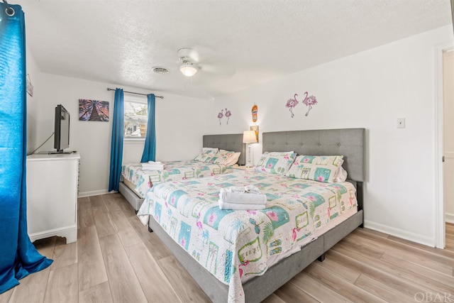 bedroom with baseboards, visible vents, a textured ceiling, and light wood finished floors