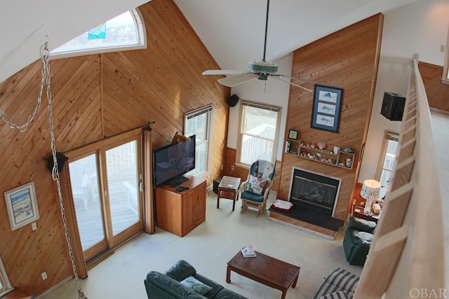 living area with high vaulted ceiling, carpet flooring, a glass covered fireplace, and wooden walls