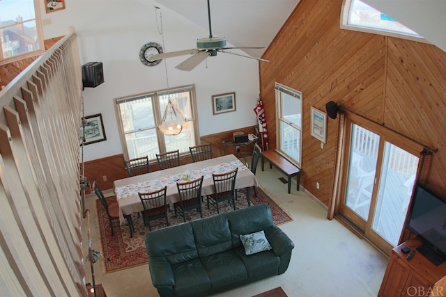 carpeted dining space featuring a wainscoted wall, high vaulted ceiling, a ceiling fan, and wooden walls