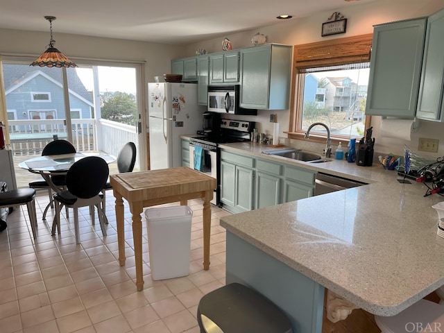 kitchen featuring stainless steel appliances, light countertops, hanging light fixtures, a sink, and a kitchen bar