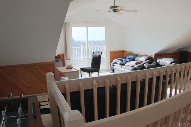 living area with a wainscoted wall, ceiling fan, wood walls, and vaulted ceiling