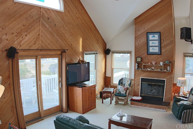 carpeted living area featuring wood walls, high vaulted ceiling, and a glass covered fireplace