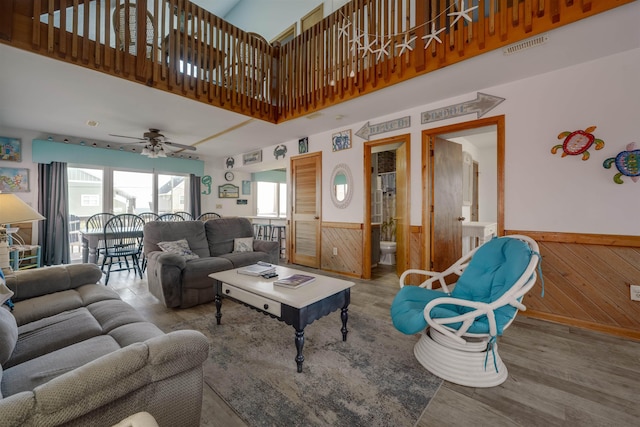 living area with a towering ceiling, wainscoting, ceiling fan, wood walls, and wood finished floors