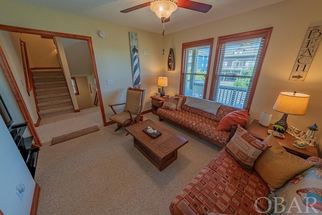 carpeted living room with ceiling fan and stairs