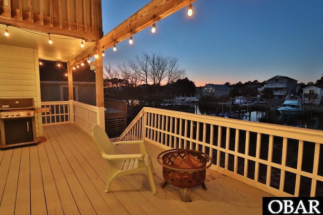 deck at dusk with a water view, a grill, and a fire pit