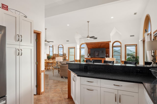 kitchen featuring light tile patterned floors, white cabinets, a ceiling fan, dark countertops, and open floor plan