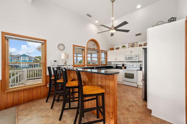 kitchen featuring a breakfast bar, dark countertops, white cabinetry, white appliances, and a peninsula