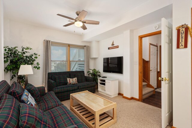 living area featuring ceiling fan, stairs, baseboards, and light colored carpet