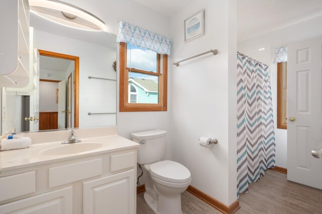 bathroom with a shower with shower curtain, toilet, vanity, wood finished floors, and baseboards