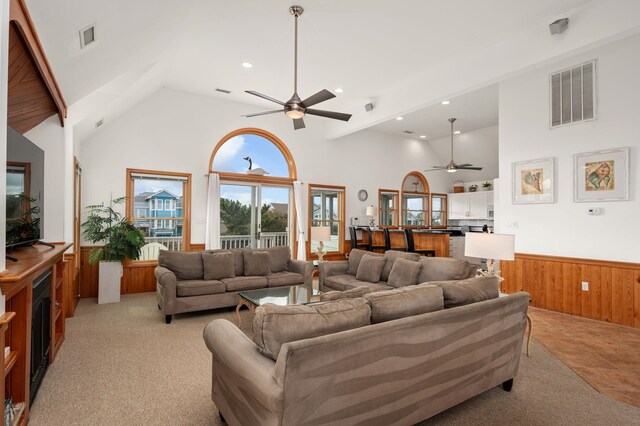 living area featuring a wainscoted wall, high vaulted ceiling, visible vents, and wooden walls