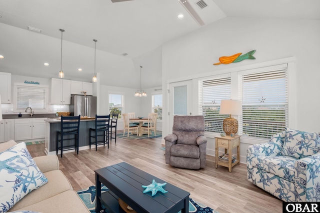 living area featuring high vaulted ceiling, light wood finished floors, a chandelier, and visible vents
