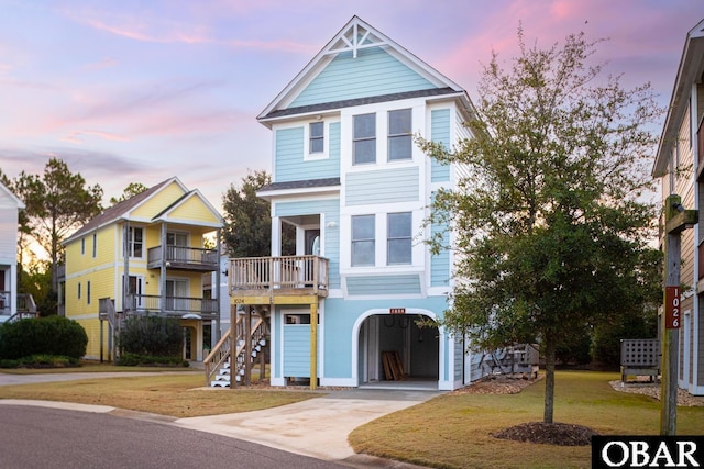 raised beach house with concrete driveway, stairway, a front yard, a balcony, and a carport