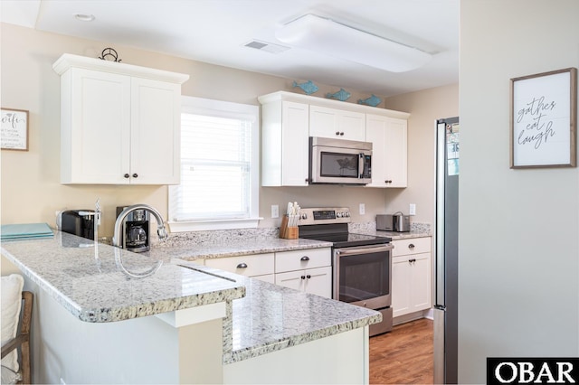 kitchen featuring a peninsula, a breakfast bar, visible vents, white cabinetry, and appliances with stainless steel finishes