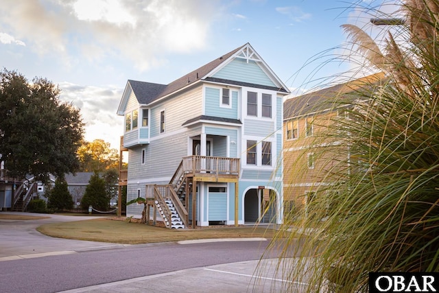 coastal inspired home featuring roof with shingles, stairway, and a front yard