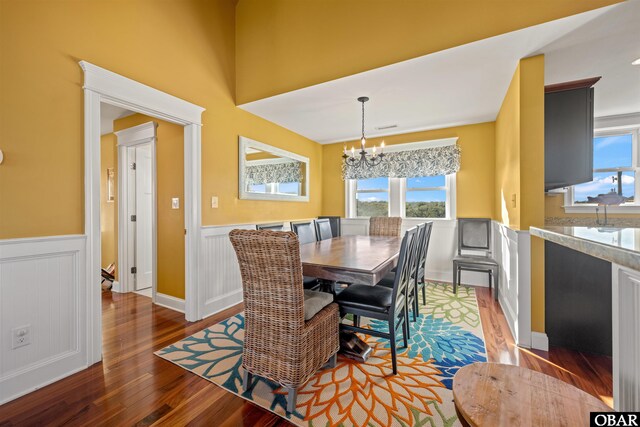 dining space featuring dark wood-type flooring, wainscoting, and a notable chandelier