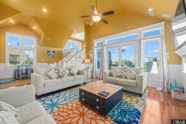 living room with stairs, high vaulted ceiling, wood finished floors, and wainscoting