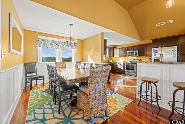 dining area featuring a wainscoted wall, wood finished floors, visible vents, and lofted ceiling