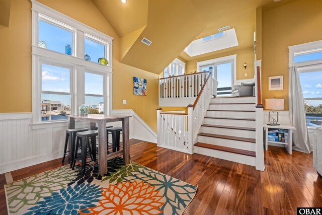 stairs featuring high vaulted ceiling, wainscoting, visible vents, and wood finished floors