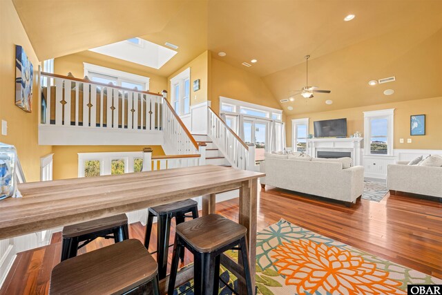 dining space featuring visible vents, wood finished floors, stairs, a fireplace, and high vaulted ceiling