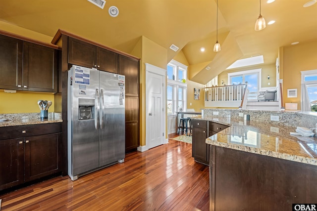 kitchen with light stone counters, pendant lighting, lofted ceiling, dark brown cabinets, and stainless steel fridge