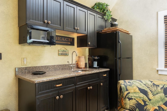 kitchen with a textured wall, dark cabinetry, a sink, and black appliances