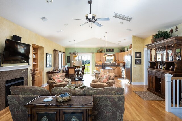 living area with vaulted ceiling, visible vents, a fireplace, and light wood finished floors