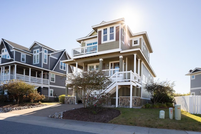 view of front of property with covered porch, fence, a balcony, driveway, and a front lawn