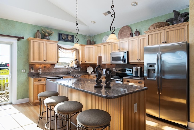 kitchen featuring lofted ceiling, a kitchen island, appliances with stainless steel finishes, decorative light fixtures, and backsplash