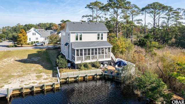 rear view of house featuring a water view, a sunroom, and a shingled roof