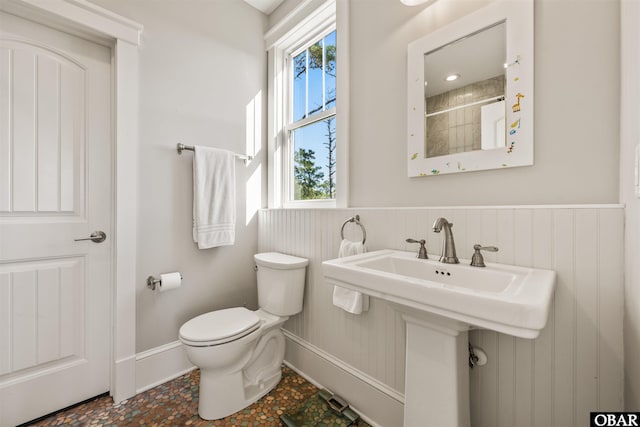 bathroom with curtained shower, toilet, baseboards, and a wainscoted wall