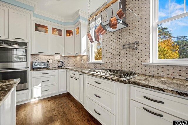 kitchen featuring backsplash, dark stone counters, appliances with stainless steel finishes, a toaster, and glass insert cabinets