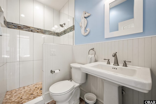 bathroom featuring a tile shower, wainscoting, and toilet