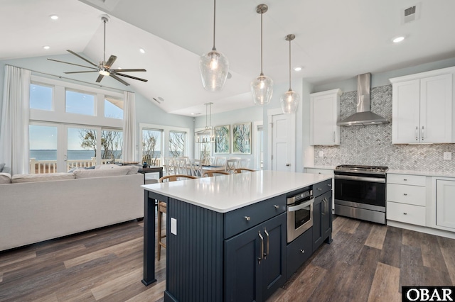 kitchen featuring dark wood-style flooring, stainless steel appliances, open floor plan, white cabinets, and wall chimney range hood