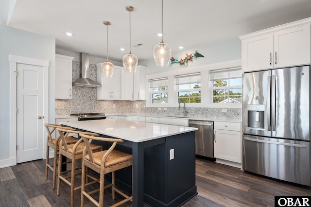 kitchen with appliances with stainless steel finishes, light countertops, wall chimney range hood, and decorative backsplash