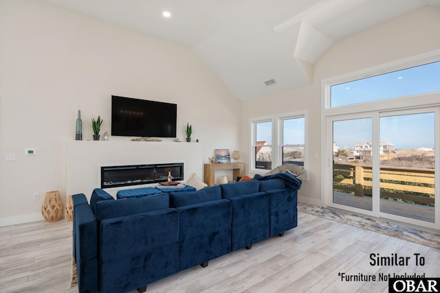 living room with high vaulted ceiling, light wood finished floors, a glass covered fireplace, and visible vents