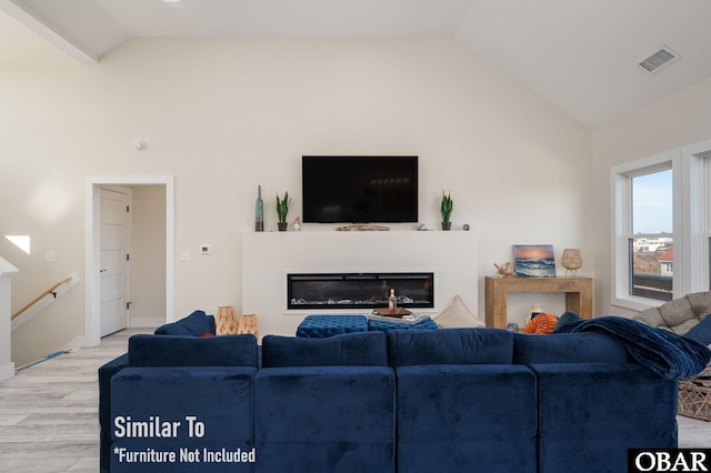 living room with high vaulted ceiling, light wood finished floors, a glass covered fireplace, and visible vents