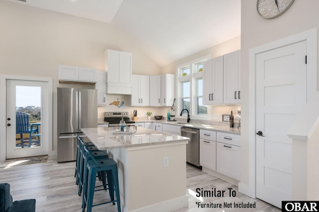 kitchen featuring white cabinets, appliances with stainless steel finishes, a kitchen breakfast bar, a center island, and a sink