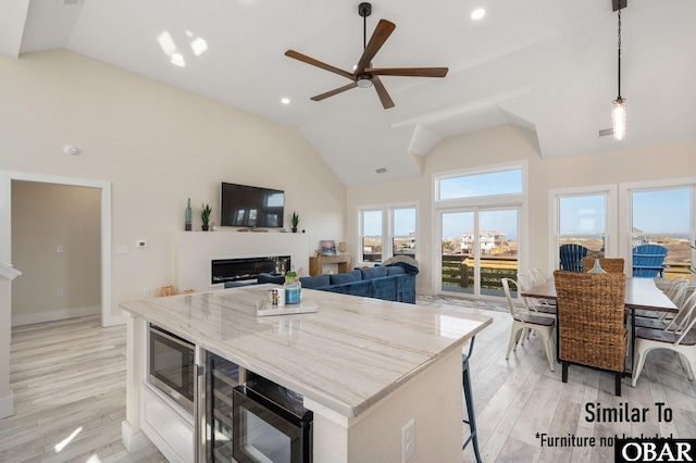 kitchen with light stone counters, light wood-type flooring, a glass covered fireplace, and pendant lighting