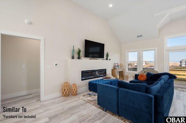 living room with baseboards, visible vents, a glass covered fireplace, vaulted ceiling, and light wood-style floors