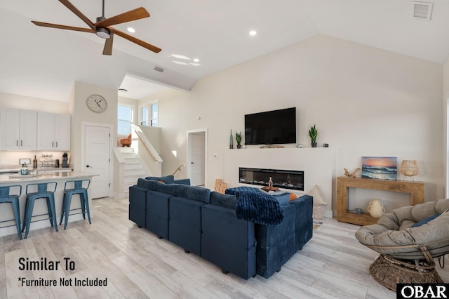 living room featuring light wood finished floors, stairs, visible vents, and a glass covered fireplace