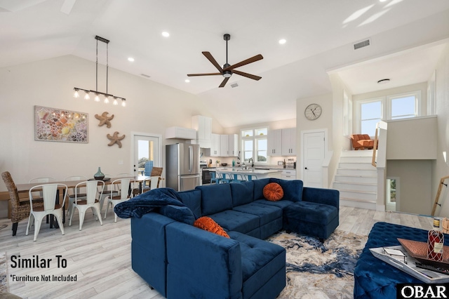 living area with high vaulted ceiling, a ceiling fan, visible vents, light wood-style floors, and stairway