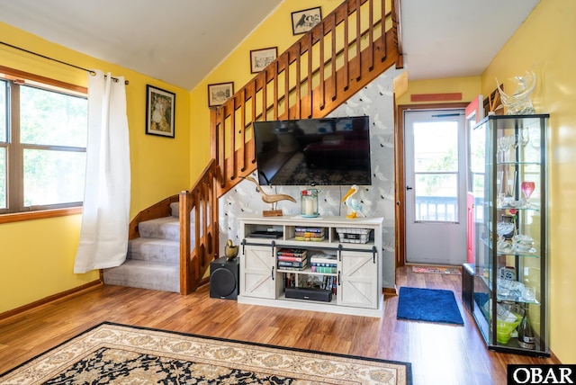 living area with stairway, plenty of natural light, wood finished floors, and lofted ceiling