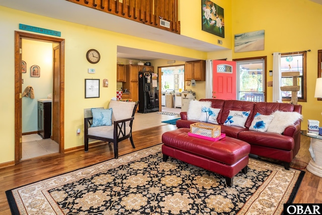 living area with baseboards, light wood-style flooring, and a towering ceiling