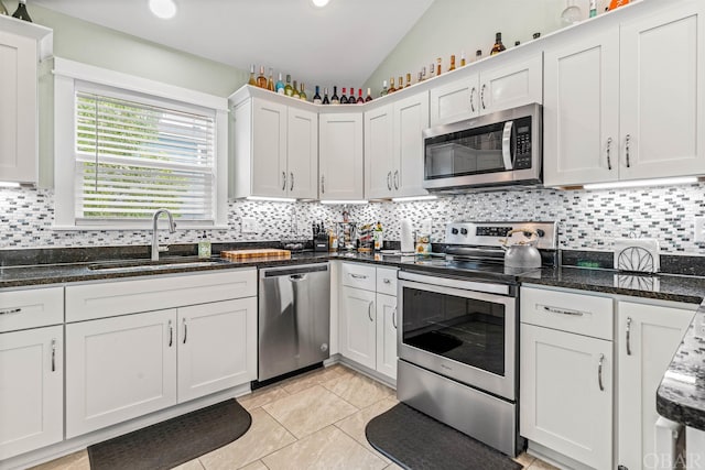 kitchen with stainless steel appliances, a sink, white cabinets, vaulted ceiling, and dark stone countertops